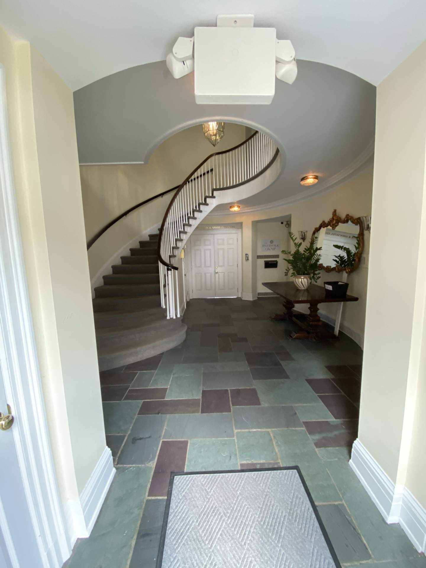 The grand foyer of The Phillips Mansion — curved staircase with original banister, slate tile floors, and ornate gilded mirror